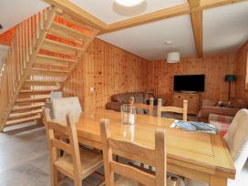 A dining table with chairs and a glass candle holder in a wooden paneled room with stairway and sofas at Bradan Lodge in Dalmally