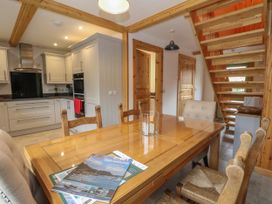 A dining area with a wooden table and chairs next to a kitchen with white cabinets and wooden stairs in the background at Bradan Lodge in Dalmally