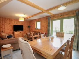 A dining area with a wooden table and chairs next to a living room with sofas and a television at Bradan Lodge in Dalmally