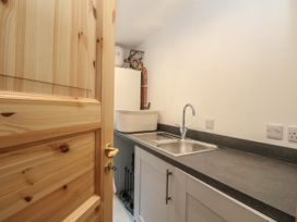 A utility room with a stainless steel sink a white basket on the counter and visible plumbing behind a wooden door at Bradan Lodge in Dalmally