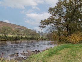 A river flowing beside a grassy bank with trees and hills in the background at Bradan Lodge in Dalmally