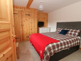 A bedroom with a double bed plaid bedding wooden wardrobes a dresser with a television and a wooden door at Bradan Lodge in Dalmally