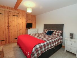 A bedroom with a bed a red blanket a white chest of drawers with a television and a white nightstand with a lamp at Bradan Lodge in Dalmally