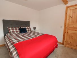 A bedroom with a double bed with plaid bedding a red blanket a dark gray headboard a wooden door and a small white bedside table with a lamp at Bradan Lodge in Dalmally