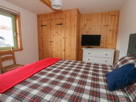 A bedroom with a bed covered in plaid bedding a wooden chair a white dresser with a television and wooden paneling on the walls at Bradan Lodge in Dalmally