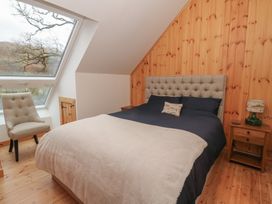 A bedroom with a bed chair wooden side table and large slanted window at Bradan Lodge in Dalmally