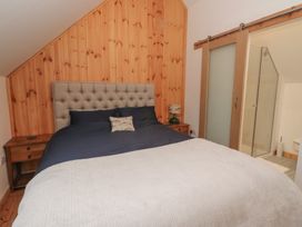 A bedroom with a large bed a wooden headboard bedside tables and an adjoining bathroom with a sliding door at Bradan Lodge in Dalmally