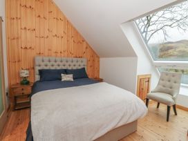 A bedroom with a double bed a wooden paneled wall a bedside table a chair and a large window at Bradan Lodge in Dalmally