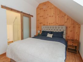 A bedroom with a bed with a gray headboard and navy bedding next to a wooden nightstand and a sliding wooden door leading to a bathroom at Bradan Lodge in Dalmally