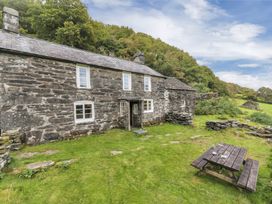 Stone cottage with white framed windows and a wooden picnic table on a grassy area at Tan Y Clogwyn in Dolwyddelan near Betws-Y-Coed