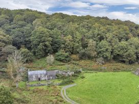 A stone house with a slate roof surrounded by grass and trees at Tan Y Clogwyn in Dolwyddelan near Betws-Y-Coed