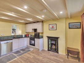 A kitchen with white cabinets, black countertop, dishwasher, oven, small fireplace, two framed pictures, and wooden floor at Tan Y Clogwyn in Dolwyddelan near Betws-Y-Coed