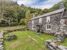 Stone cottage with white windows and wooden picnic table in grassy yard surrounded by stone walls at Tan Y Clogwyn in Dolwyddelan near Betws-Y-Coed