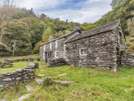 A stone cottage with stone walls and grass yard surrounded by trees at Tan Y Clogwyn in Dolwyddelan near Betws-Y-Coed