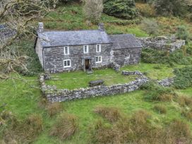 An old stone cottage with a slate roof surrounded by a low stone wall and green grass at Tan Y Clogwyn in Dolwyddelan near Betws-Y-Coed