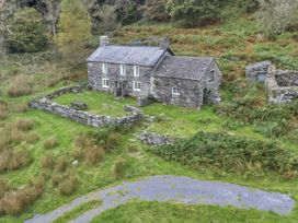 A stone cottage with a fenced yard and picnic table surrounded by grass and trees at Tan Y Clogwyn in Dolwyddelan near Betws-Y-Coed