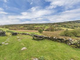A grassy outdoor area with a stone wall and picnic table overlooking countryside fields and trees at Tan Y Clogwyn in Dolwyddelan near Betws Y Coed
