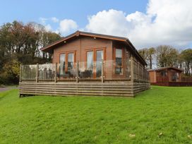 A wooden lodge with glass railing on a grassy hill with trees in the background at Lakeview Lodge in Forton near Garstang