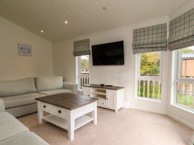 A living room with a sofa coffee table tv and windows with checkered blinds at Lakeview Lodge in Forton near Garstang