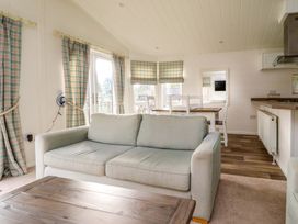 A living room with a sofa, wooden table, dining table with chairs, and windows with plaid curtains at Lakeview Lodge in Forton near Garstang