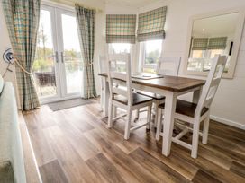 A dining area with a wooden table and four chairs near windows and glass doors with plaid curtains at Lakeview Lodge in Forton near Garstang