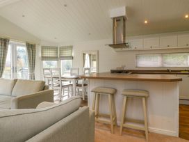 An open kitchen and living area with bar stools a dining table and chairs and a sofa at Lakeview Lodge in Forton near Garstang