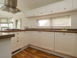 A kitchen with white cabinets a gas stove and a window with blinds at Lakeview Lodge in Forton near Garstang