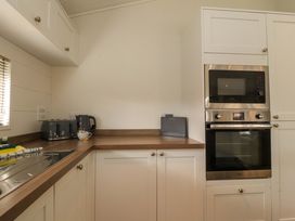A kitchen corner with white cabinets a countertop a toaster a kettle a mug a microwave and an oven at Lakeview Lodge in Forton near Garstang