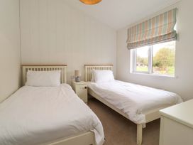 A bedroom with two single beds a small bedside table lamp and a window with striped blinds at Lakeview Lodge in Forton near Garstang