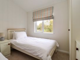 A bedroom with a single bed next to a window with striped blinds and a bedside table with a lamp at Lakeview Lodge in Forton near Garstang