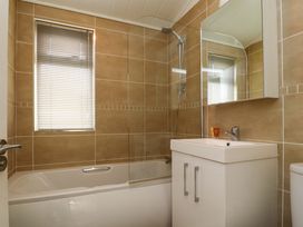 A bathroom with a bathtub shower combination a sink with cabinet and mirror and a window with blinds at Lakeview Lodge in Forton near Garstang