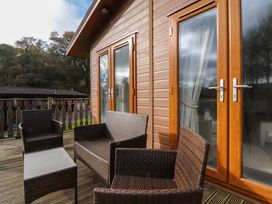 A wooden deck with outdoor wicker chairs and a table outside a building with double glass doors at Lakeview Lodge in Forton near Garstang