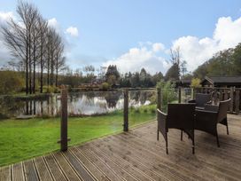 A wooden deck with chairs overlooking a small lake and trees at Lakeview Lodge in Forton near Garstang