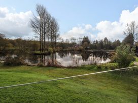 A pond surrounded by trees and grass with a house in the background at Lakeview Lodge in Forton near Garstang