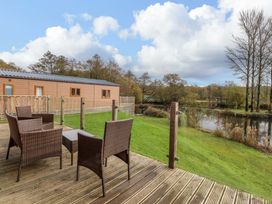 A wooden deck with wicker chairs and a table overlooking a grassy area and a pond at Lakeview Lodge in Forton near Garstang