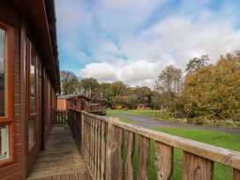A wooden deck with railing outside wooden cabins in a green area with trees at Lakeview Lodge in Forton near Garstang