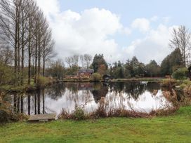 A pond surrounded by trees and grass with a house in the background at Lakeview Lodge in Forton near Garstang