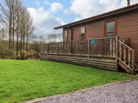 A cabin with a wooden deck and railing overlooking a grassy yard and trees at Lakeview Lodge in Forton near Garstang