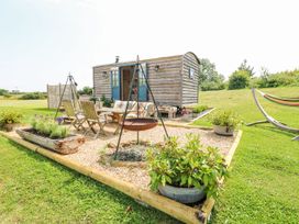 A wooden shepherds hut with blue doors next to a gravel seating area with chairs and plants and a hammock in a grassy outdoor space at Lillies Shepherds Hut at Shepherds Lodge in Bottesford near Redmile and Vale of Belvoir