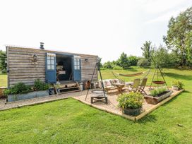 A wooden shepherds hut with blue doors in a garden with outdoor seating a hammock and plants at Lillies Shepherds Hut at Shepherds Lodge Bottesford near Redmile and Vale of Belvoir