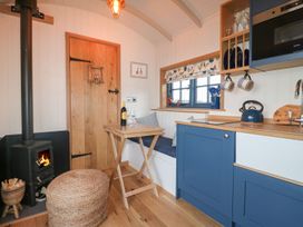 A small kitchen with blue cabinets a wooden table a wood burning stove and a cushioned bench under a window at Lillies Shepherds Hut at Shepherds Lodge Bottesford near Redmile and Vale of Belvoir
