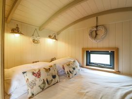 A bedroom with a bed with chicken patterned pillows and small window with a heart decoration on the wall at Lillies Shepherds Hut at Shepherds Lodge Bottesford near Redmile and Vale of Belvoir