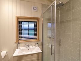 A bathroom with a sink and faucet under a window with blinds and a shower with glass door and tiled walls at Lillies Shepherds Hut at Shepherds Lodge Bottesford near Redmile and Vale of Belvoir