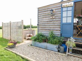 An outdoor area with a wooden cabin having a blue door a metal planter with green plants a watering can and a wooden hot tub behind a slatted wooden screen at Lillie's Shepherds Hut at Shepherds Lodge Bottesford near Redmile and Vale of Belvoir