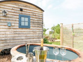 An outdoor hot tub with a bottle of champagne in an ice bucket and two empty wine glasses next to a wooden building and garden at Lillie's Shepherds Hut at Shepherds Lodge Bottesford near Redmile and Vale of Belvoir