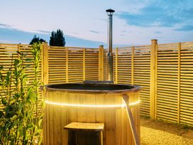 A wooden outdoor hot tub with a metal chimney and string lights next to a wooden fence at Lillies Shepherds Hut at Shepherds Lodge in Bottesford near Redmile and Vale of Belvoir