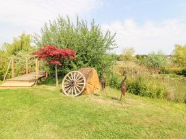 A grassy garden area with a wooden wagon wheel, a rock, metal bird sculptures, and a wooden bridge over water at Lillie's Shepherds Hut at Shepherds Lodge in Bottesford near Redmile and Vale of Belvoir