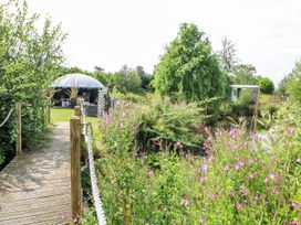 A wooden bridge over a small body of water with pink flowers and green trees near a yurt at Lillie's Shepherds Hut at Shepherds Lodge Bottesford near Redmile and Vale of Belvoir