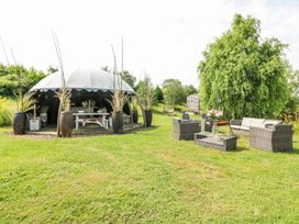 A dome tent with dining table and benches next to outdoor wicker seating with glass table on grass at Lillie's Shepherds Hut at Shepherds Lodge in Bottesford near Redmile and Vale of Belvoir