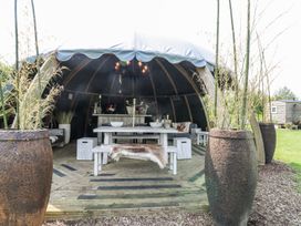 An outdoor wooden pavilion with a table, benches, stools, plants in large pots, and seating at Lillie's Shepherds Hut at Shepherds Lodge in Bottesford near Redmile and Vale of Belvoir